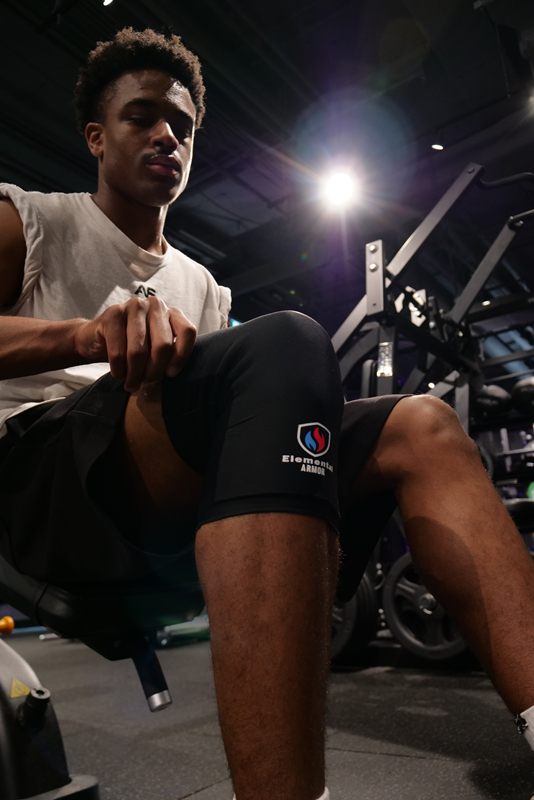 Athlete adjusting an Elemental Armor Knee Sleeve on a gym bench