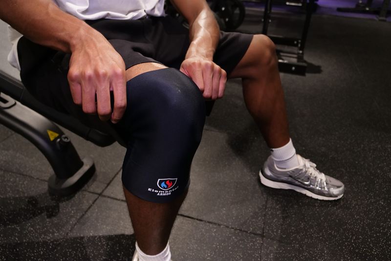 Athlete seated on a gym bench wearing the Knee Sleeve