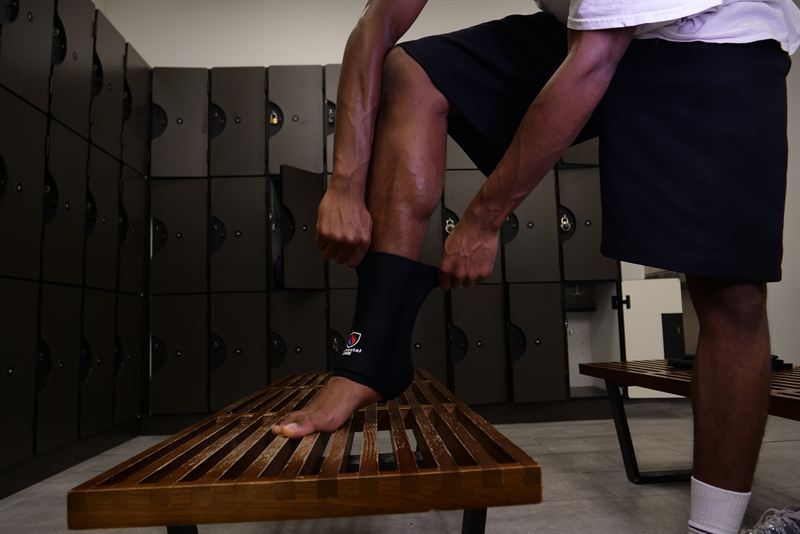 Athlete pulling on the Elemental Armor Ankle Sleeve in a locker room